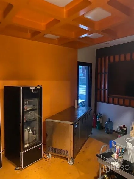 店屋 出租 - 服务间橙色天花，玻璃门冰箱与不锈钢工作台。