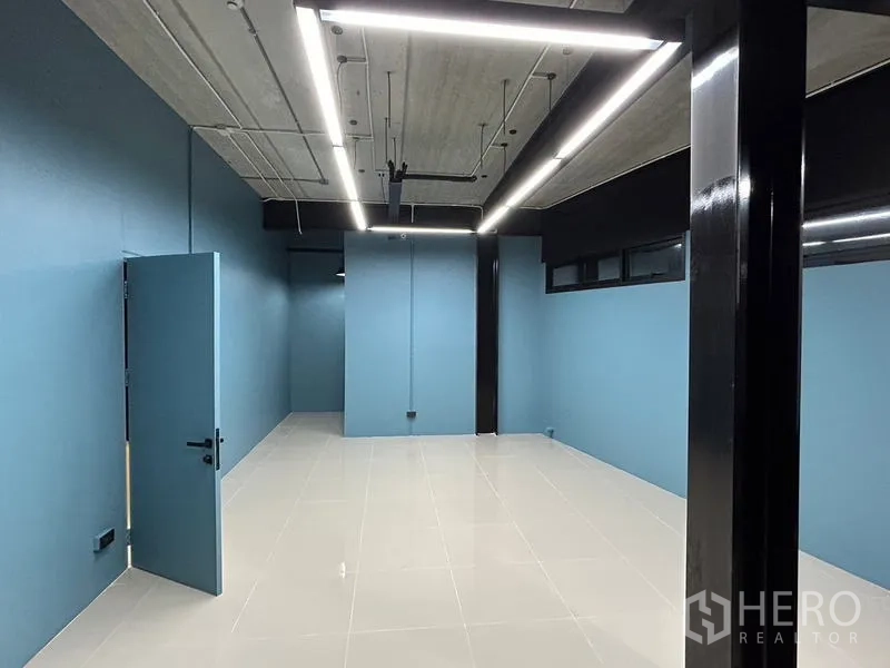 Office Space for rent in Chatuchak, Bangkok - Long rectangular office area with blue walls, black beams, suspended linear LEDs and shiny ceramic floors.