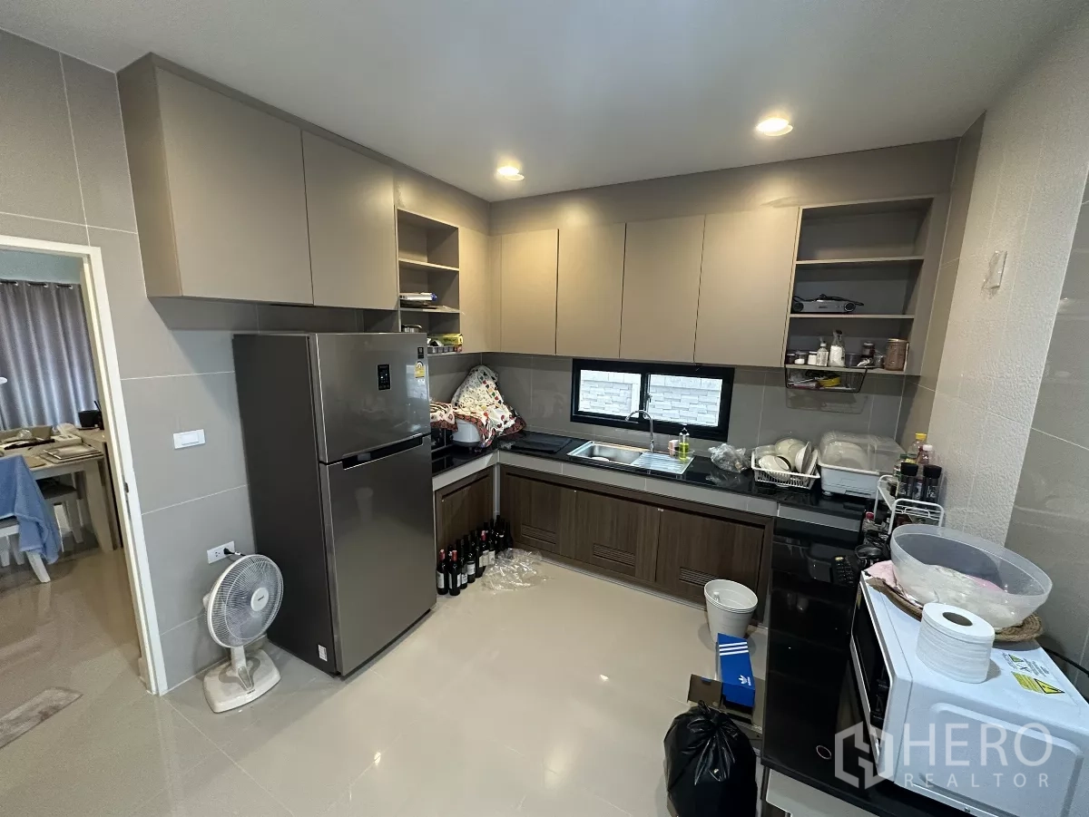 Detached House for rent or sale in Lam Luk Ka, Pathum Thani - U-shaped kitchen featuring upper and lower cabinets, double windows, refrigerator and tiled walls.