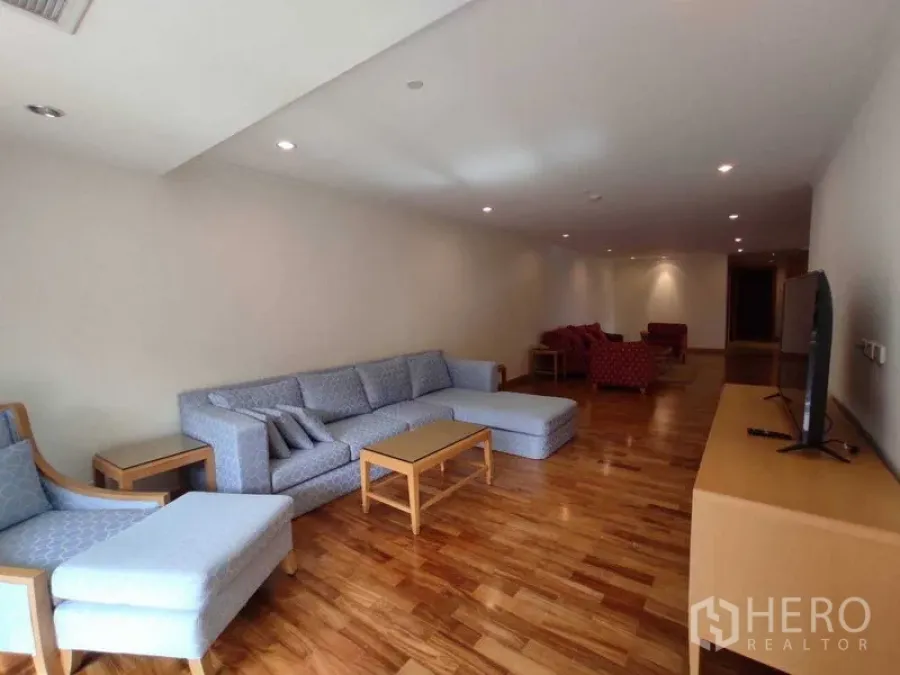 Condominium for rent in Khlong Toei, Bangkok - Long open‑plan lounge with large sofa set and additional red armchairs at the far end.