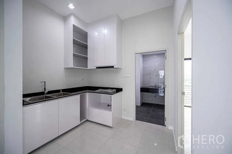 Home Office for rent in Suan Luang, Bangkok - L-shaped pantry with white cabinets and black counters located next to a bathroom doorway.