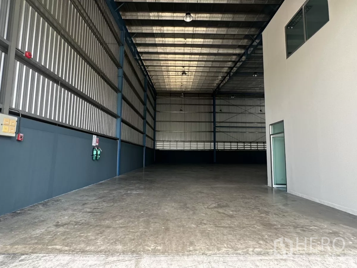Factory for rent in Bang Phli, Samut Prakan - View from warehouse entrance toward deep storage area with emergency equipment on the wall.