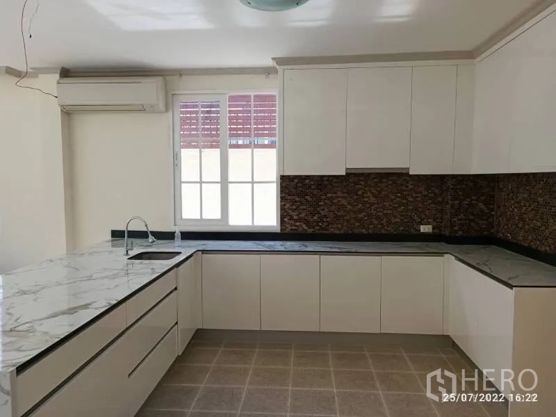 Detached House for sale in Prawet, Bangkok - Modern L-shaped kitchen with white cabinetry, marble-look counters and window.