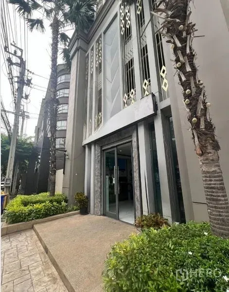 Retail Space for rent in Khlong Toei, Bangkok - Entrance of the retail space showing a tall glass doorway, landscaped planters, sidewalk, and palm trees along the frontage in Khlong Toei.