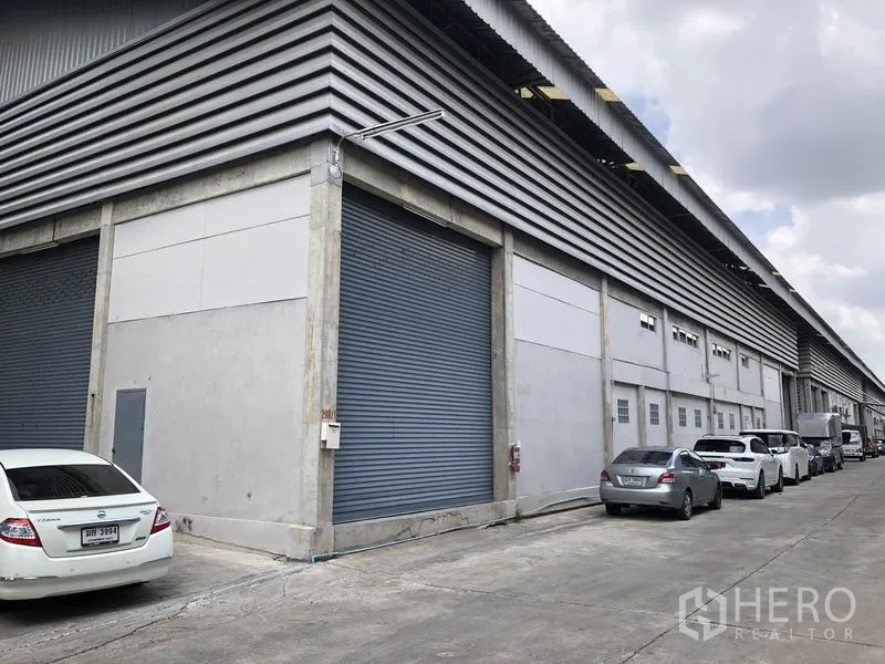 Warehouse for rent in Khlong Sam Wa, Bangkok - Long side of the warehouse showing several loading bay roller shutters and a wide truck-friendly driveway.