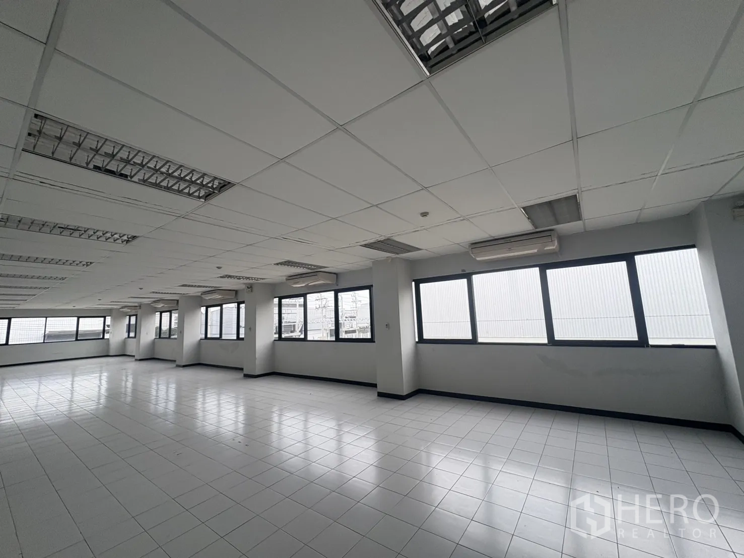 Factory for rent or sale in Samut Prakan - Spacious office area with grid ceiling, fluorescent lighting and windows.