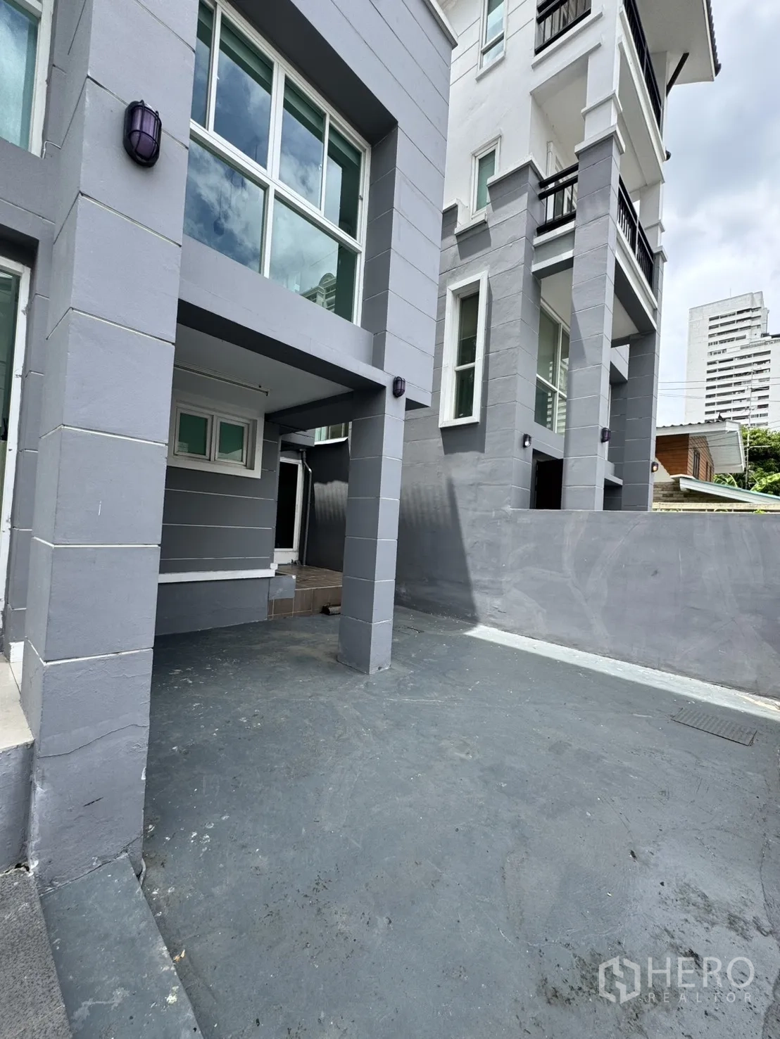 Home Office for rent in Watthana, Bangkok - Ground-floor covered carport and main entry beneath a gray facade.