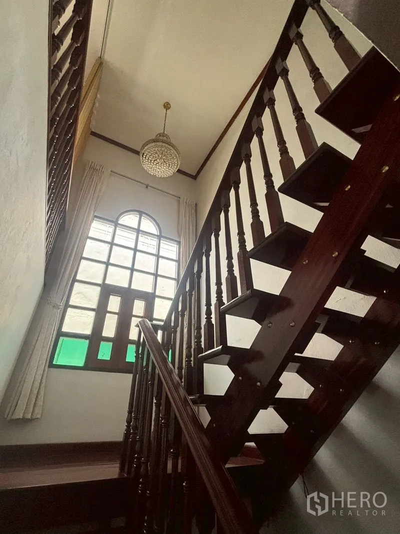 Detached House for sale in Suan Luang, Bangkok - Wooden staircase detail beneath high ceiling and arched window.