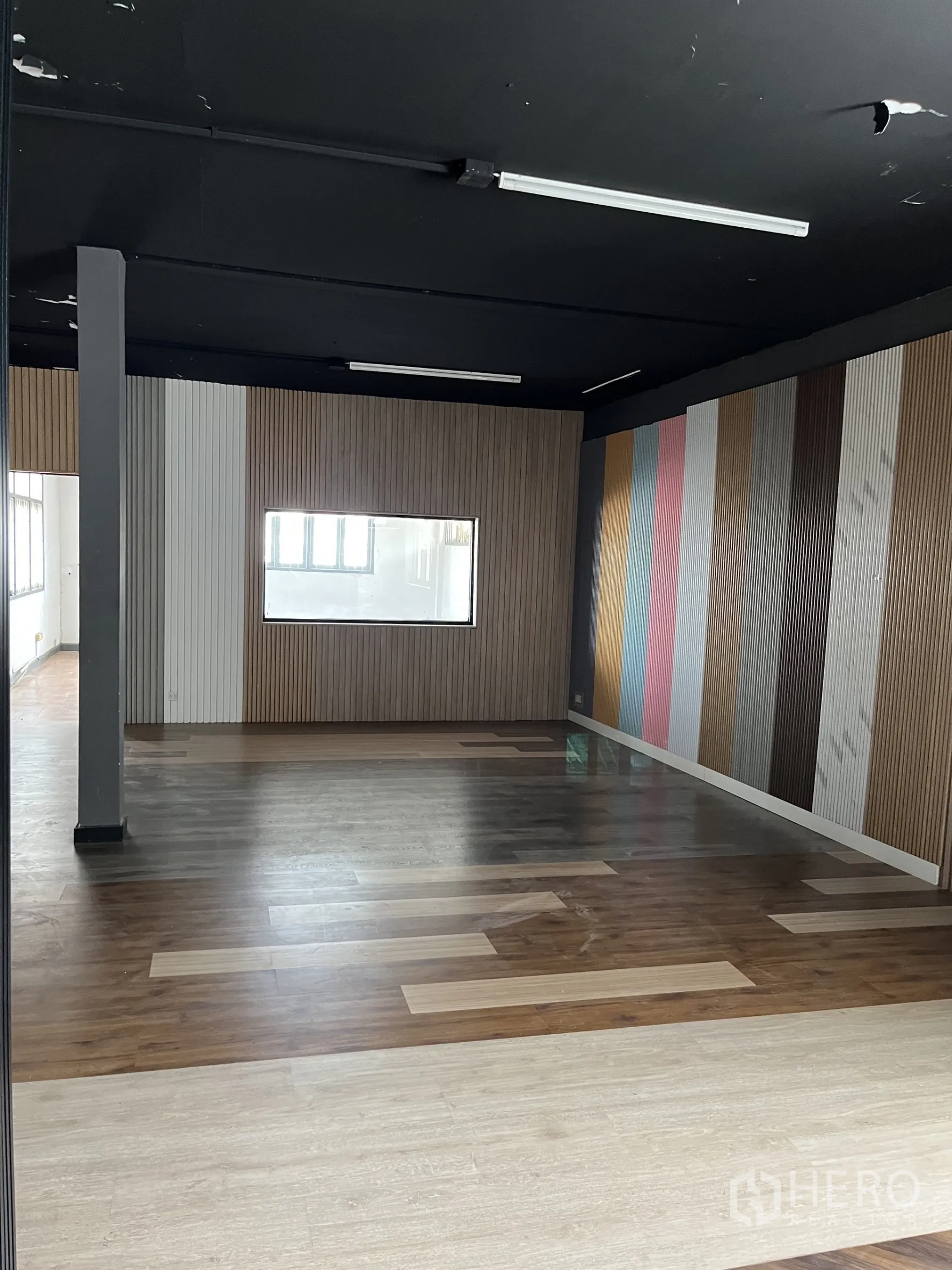 Warehouse for rent in Bangkok - Open office-style room with black ceiling, wood-slat accent walls and mixed laminate flooring.
