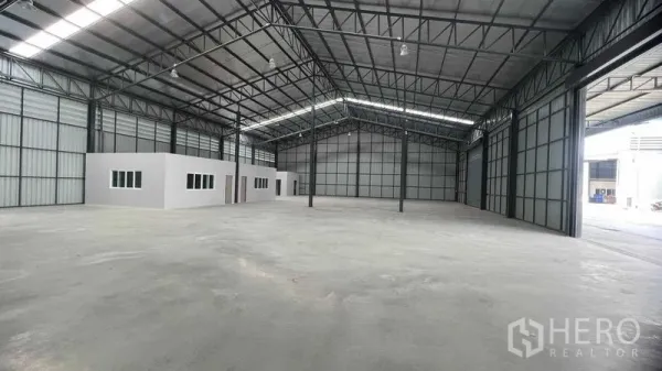 Warehouse for rent in Pathum Thani - Open warehouse interior showing skylight panels, two built-in office rooms and wide loading door openings.