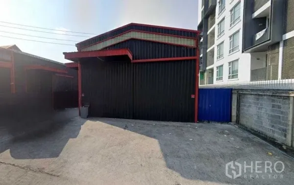 Warehouse for rent in Chatuchak, Bangkok - Front view of a black metal warehouse with red trim and a wide concrete forecourt in Chatuchak.