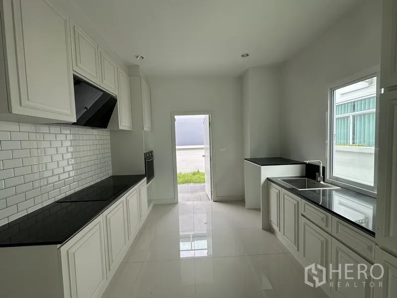 Detached House for sale in Lam Luk Ka, Pathum Thani - Closed kitchen with white cabinetry, subway tile backsplash and black countertops.