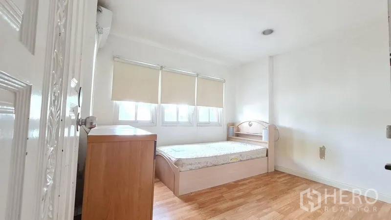 Detached House for rent in Lat Phrao, Bangkok - Cozy bedroom with laminate flooring, bedside furniture and three windows with blinds.