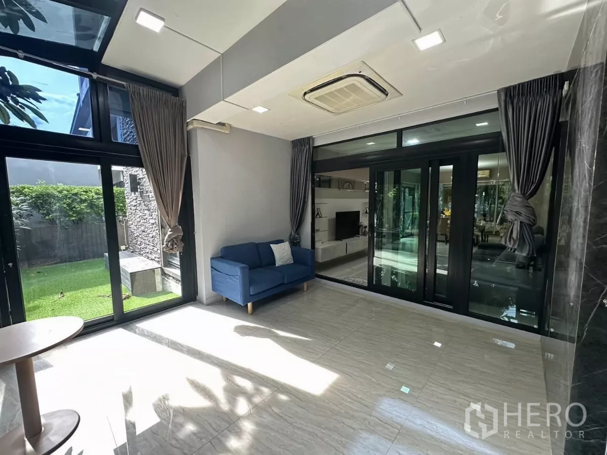 Detached House for rent or sale in Bang Kapi, Bangkok - Sunlit multipurpose room with blue sofa and floor-to-ceiling glass doors to the yard.
