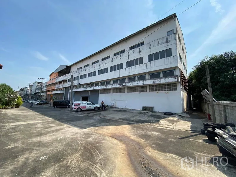 โรงงาน ขายในBang Phli, Samut Prakan - อาคารโรงงานสี่ชั้นพร้อมลานคอนกรีตกว้างและที่จอดรถ ท้องฟ้าแจ่มใส