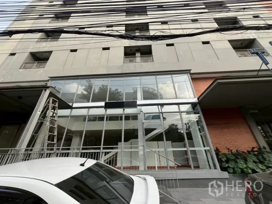 Retail Space for rent in Watthana, Bangkok - Ground-floor glass storefront of a modern mixed-use building with entry steps and parking.