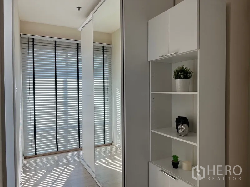 Condominium for rent in Khlong Toei, Bangkok - Bright corridor with floor‑to‑ceiling windows, sliding mirrored wardrobe and white shelving unit.