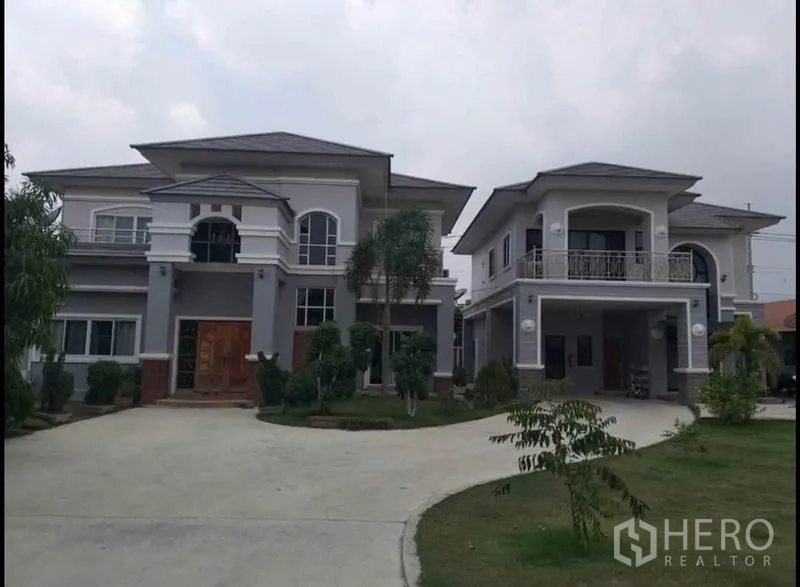 Detached House for sale in Lam Luk Ka, Pathum Thani - Wide view of both houses with landscaped lawn and curved driveway.