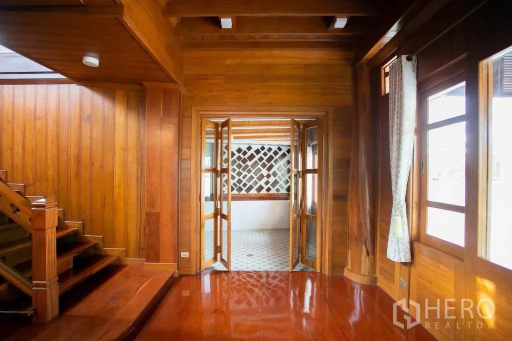 Detached House for rent or sale in Huai Khwang, Bangkok - Wooden hall opening via folding glass doors to a semi‑outdoor tiled area.