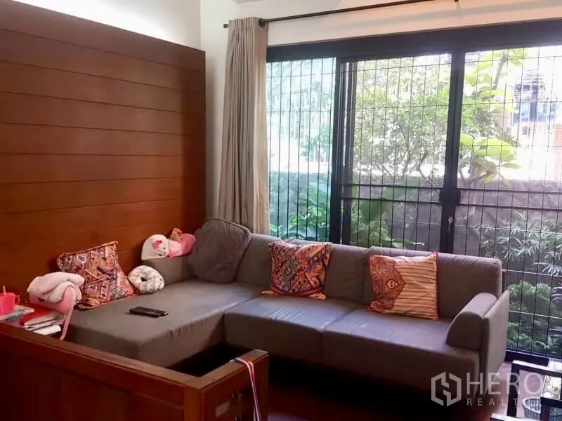 Home Office for rent or sale in Bang Rak, Bangkok - Cozy living corner with gray L-shaped sofa, sliding doors and garden outlook.