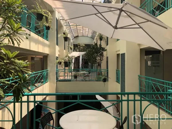 Retail Space for rent in Khlong Toei, Bangkok - Sunlit indoor atrium with green railings, plants, and café umbrellas outside the shopfront.