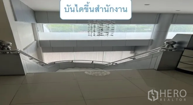 Warehouse for rent in Mueang Pathum Thani, Pathum Thani - Staircase with stainless-steel railings leading to the office floor beneath a chandelier.
