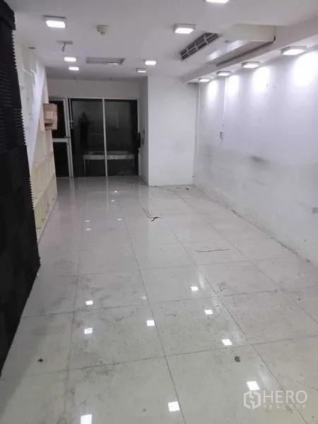 零售空间 出租在Watthana, Bangkok - 下层零售区，白色地砖、嵌入式照明以及后部玻璃门。