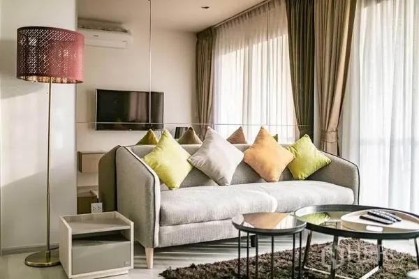 Condominium for rent in Pathum Wan, Bangkok - Bright living room with gray sofa, colorful cushions, floor lamp and TV.