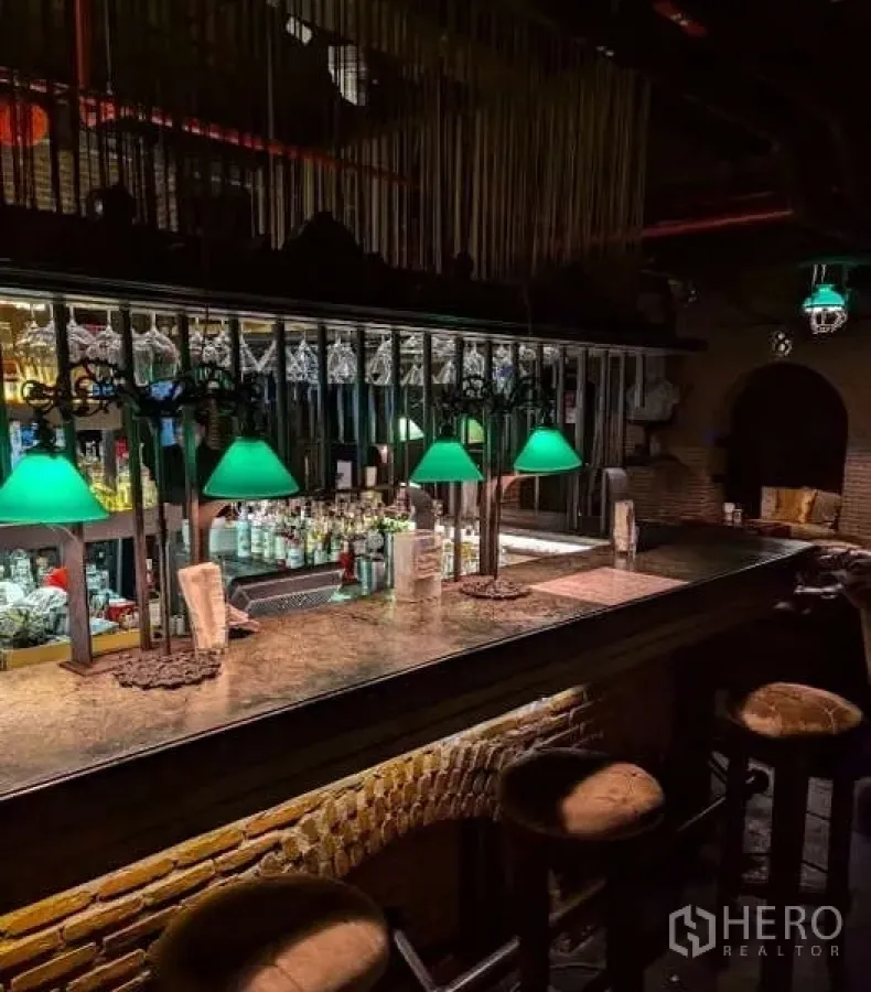 Retail Space for rent - Long bar counter with green-shaded lamps, mirrored back bar and stools in an industrial-chic venue.