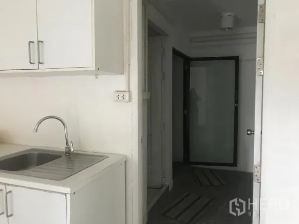 Shophouse for rent in Watthana, Bangkok - Compact pantry with white cabinets and sink beside a hallway leading to a frosted glass door.