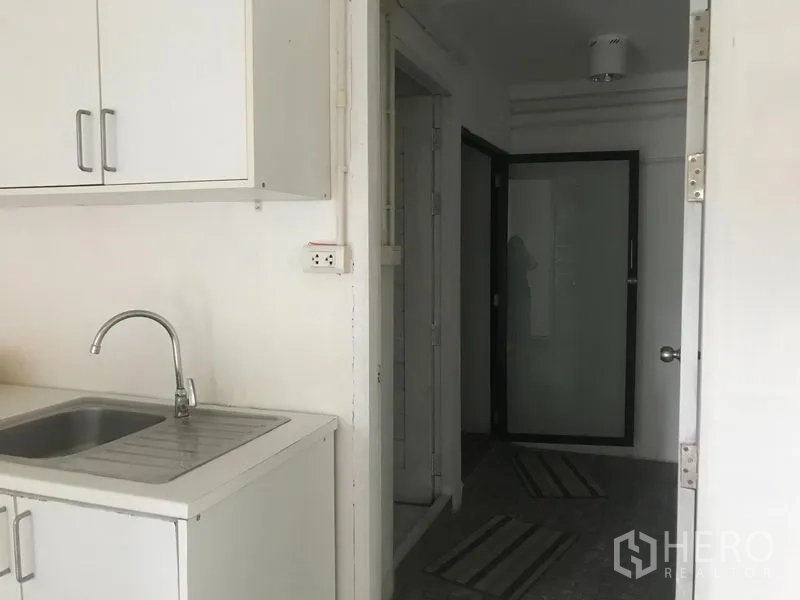 Shophouse for rent in Watthana, Bangkok - Compact pantry with white cabinets and sink beside a hallway leading to a frosted glass door.