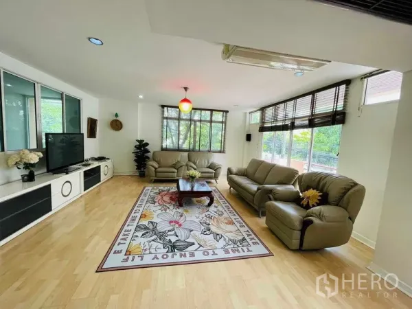 Detached House for rent in Watthana, Bangkok - Bright living room with large windows, leather sofas, and wood flooring.