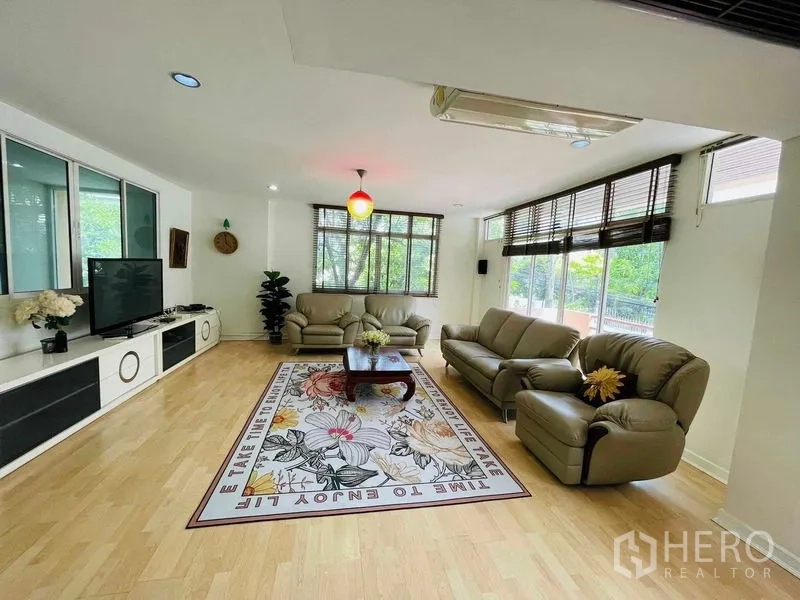 Detached House for rent in Watthana, Bangkok - Bright living room with large windows, leather sofas, and wood flooring.