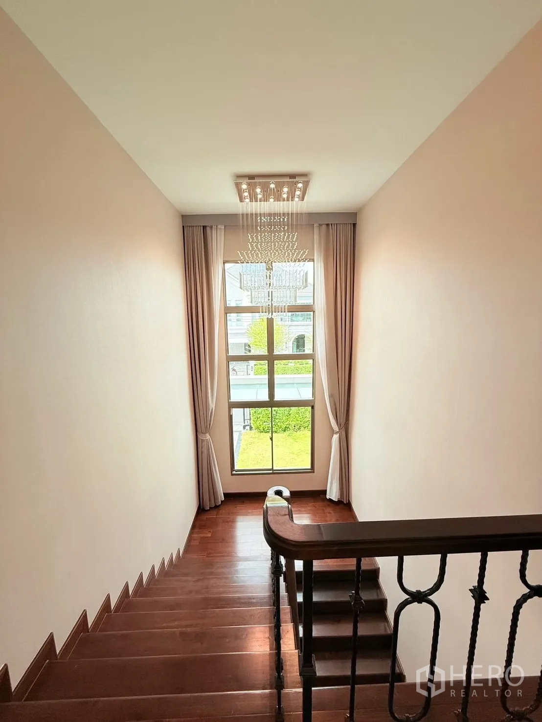 Detached House for rent or sale in Bang Phli, Samut Prakan - Staircase landing with chandelier, large window and curtains overlooking greenery.