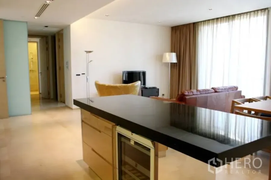 Condominium for rent in Bang Rak, Bangkok - Open-plan living area with kitchen island, TV console and seating, finished in neutral tones with full-height curtains.