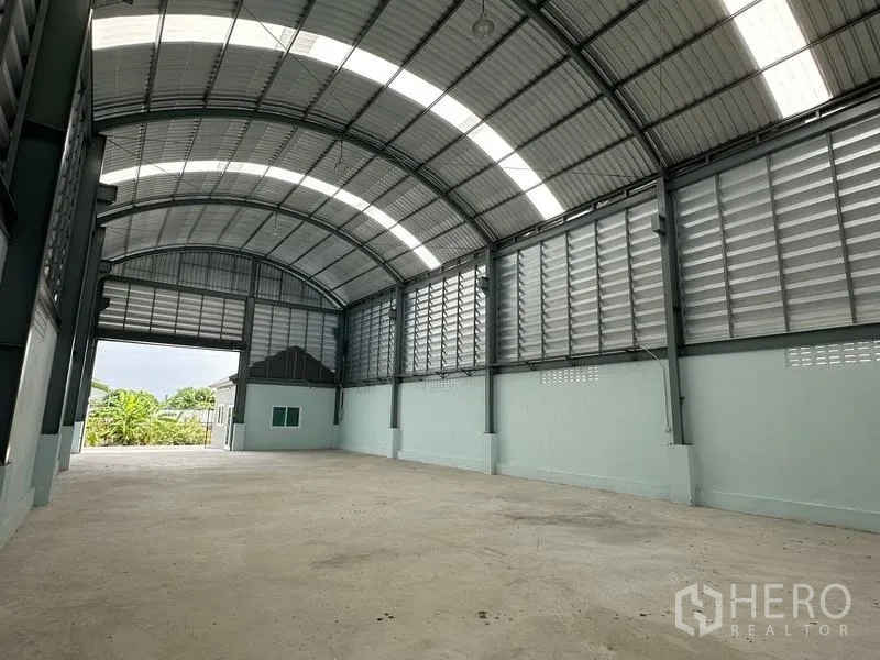 Factory for rent in Pak Kret, Nonthaburi - Interior view toward the loading entry showing clear-span space, skylight panels and concrete floor.