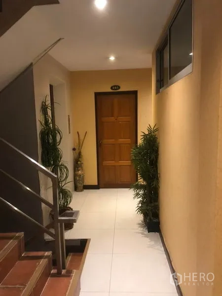 Shophouse for rent in Bang Rak, Bangkok - Interior corridor with stairway and potted plants leading to a wooden door.