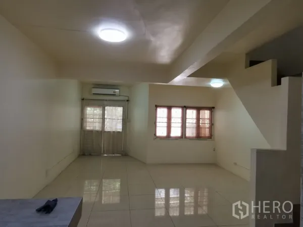 Townhouse for rent in Khlong Toei, Bangkok - Spacious living room with large windows, air conditioning, and a stairway.