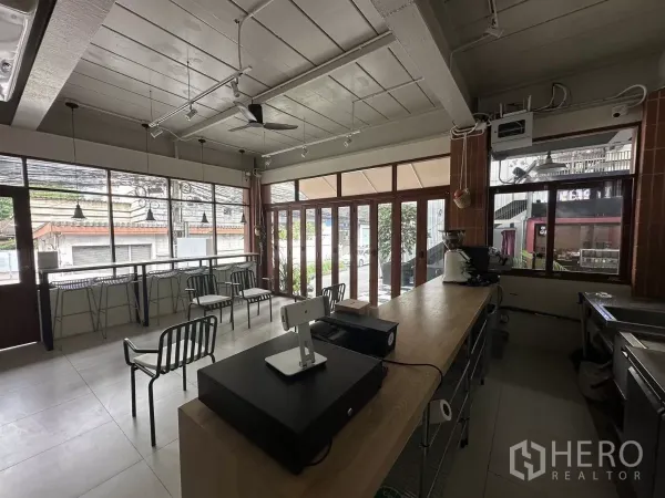 Retail Space for rent in Watthana, Bangkok - Open-plan interior with a long wooden service counter, large front windows, track and pendant lighting, and a ceiling fan.