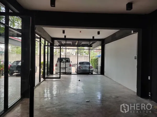 Retail Space for rent - Open-plan interior facing the parking area through floor-to-ceiling glass walls and concrete flooring.