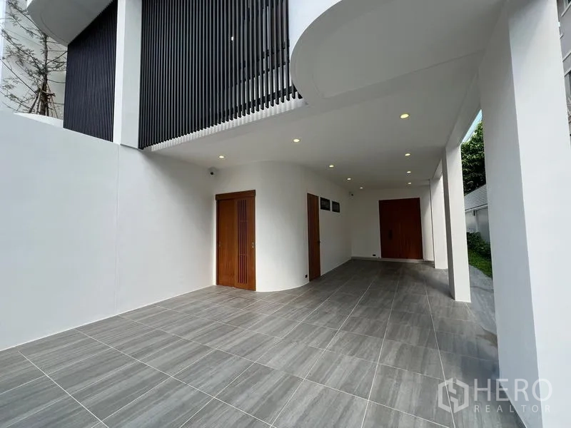 Home Office for sale in Phra Khanong, Bangkok - Covered carport beneath the building with tiled floor and wooden doors.