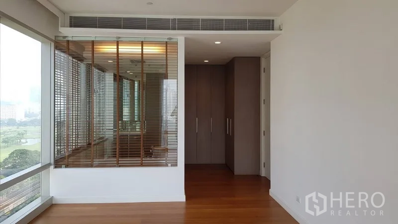 Condominium for rent in Pathum Wan, Bangkok - Bedroom with city-view window, wardrobe and glass-walled ensuite with blinds.