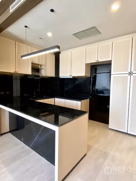 Condominium for sale in Pathum Wan, Bangkok - Modern kitchen with black stone island, light wood cabinetry, and pendant lighting.