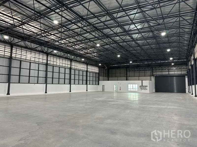 Factory for rent in Bang Sao Thong, Samut Prakan - Large warehouse hall with internal office block and a motorized roller shutter door.