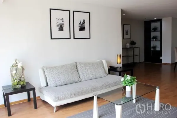 Condominium for rent in Khlong Toei, Bangkok - Bright living room with sofa, glass coffee table, framed art and wood flooring.
