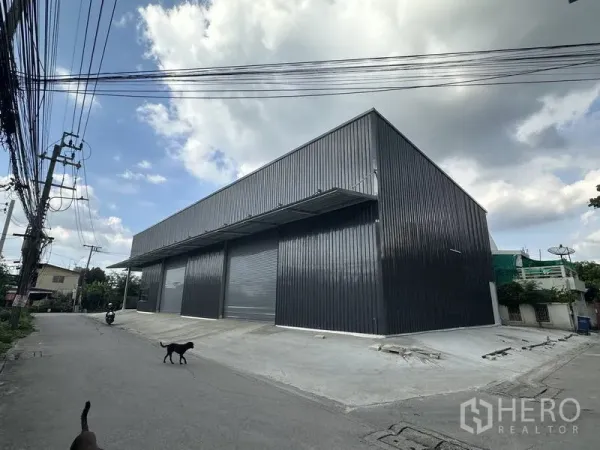 Warehouse for rent in Bang Kapi, Bangkok - Corner view of a new metal‑clad warehouse with multiple roller shutters and a loading ramp in Bang Kapi.