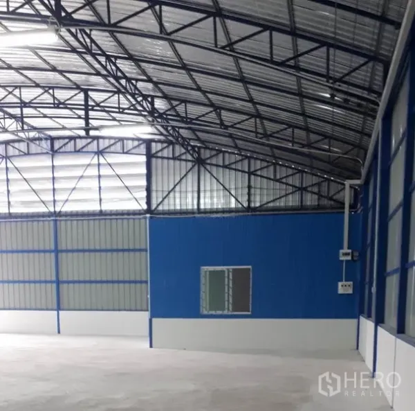 Warehouse for rent in Nong Chok, Bangkok - Spacious warehouse interior in Nong Chok, Bangkok with steel-truss roof, blue office partition and smooth concrete floor.