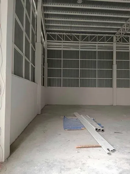 Warehouse for rent in Khlong Toei, Bangkok - High-ceiling warehouse interior with steel trusses, corrugated walls and unfinished concrete floor with materials on site.