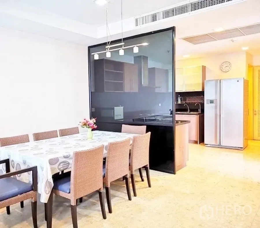 Condominium for rent in Khlong Toei, Bangkok - Open dining area with an eight‑seat table, pendant lights and a glass partition to the kitchen.