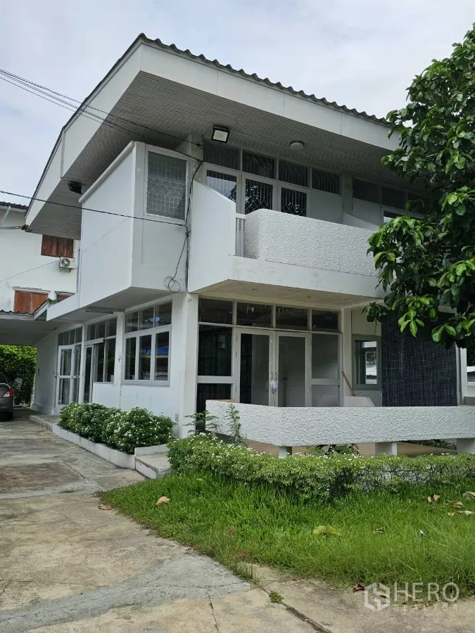 Detached House for rent or sale in Lat Phrao, Bangkok - Upper-floor balcony and wraparound windows above a covered front porch and green lawn.
